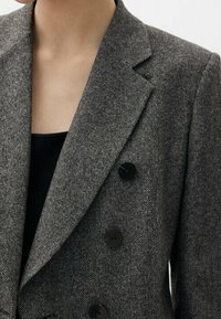Blazer a scacchi grigi con design doppiopetto, revers a punta e bottoni neri. Realizzato in tessuto testurizzato.