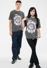 Gray graphic t-shirts featuring "THE BEACH BOYS" text and circular illustration. The male model pairs with dark jeans, while the female wears flared pants.