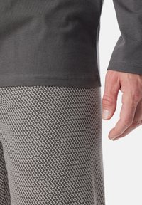 Une chemise noire à manches longues rencontre un pantalon à motifs gris clair avec un design géométrique. Gros plan d'une main contre des textures de tissu.