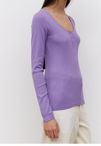 Lila långärmad topp med V-ringning och treknappsslå. Tillverkad i ribbat tyg, har den en fitted design och en mjuk textur.