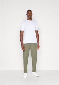 White short-sleeve t-shirt with a small logo, paired with light olive green trousers and white sneakers, set against a neutral background.
