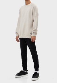 Sudadera color beige claro con mangas raglán y puños acanalados, combinada con pantalones negros ajustados y zapatillas negras con suelas blancas.