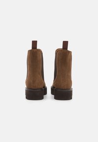 Brune suedes ankelstøvler med elastiske sidestykker, pull tabs og en tyk gummisål; har en glat overflade og minimalistisk design.