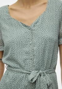 Grünes Polka-Dot-Kleid mit kurzen Ärmeln, V-Ausschnitt, Knopfleiste und einem gebundenen Gürtel in der Taille. Glattes Gewebe mit subtiler Textur.