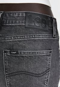 Jeans in denim nero con una finitura testurizzata, dotati di un'etichetta in pelle con "Lee" alla vita e un piccolo tag sulla tasca.