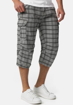 Shorts cargo à carreaux gris avec une coupe au genou, featuring des poches latérales et des carrés entourés de noir ; portés avec des baskets blanches.