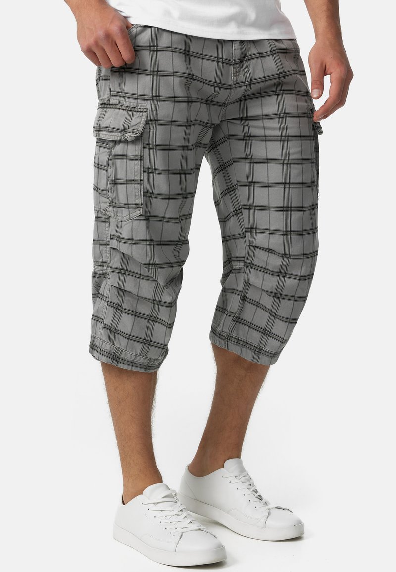 Grå plaid cargo shorts i knælang længde, med sidelommer og sorte rammede firkanter; båret med hvide sneakers.