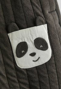 Tumehall pinnatud kangas, millel on õmmeldud valge panda näo tepitud plekk, millel on mustad silmad, nina, naeratav suu ja kaks väikest kõrva.