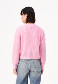 Rosa strikket genser med avslappet passform, med ribbestrikkede mansjetter og nederkant, brukt sammen med lyseblå jeans prydet med subtile sølvdetaljer.