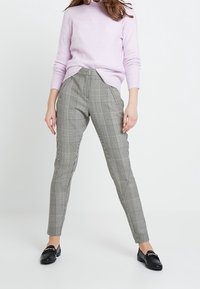 Pantalon à carreaux gris avec une coupe ajustée, taille haute, texture subtile et poches latérales. Associé à un pull violet clair et des mocassins noirs.