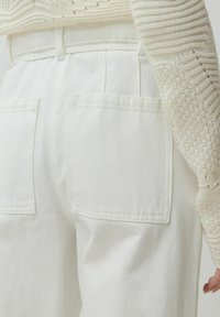 Witte denim broek met een hoge taille, met twee achterzakken en een gedeeltelijk zichtbare textuurcrème gebreide trui.