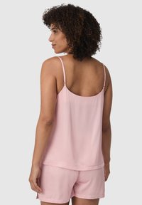 Jasnoróżowa jedwabna koszulka na ramiączkach z regulowanymi paskami, o luźnym kroju i gładkiej fakturze, w zestawie z dopasowanymi szortami.