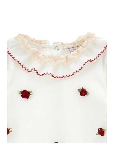 Top di tessuto bianco con colletto in pizzo, dettagli ondulati rossi e piccole applicazioni di rose rosse con foglie verdi distribuite in tutto il capo.