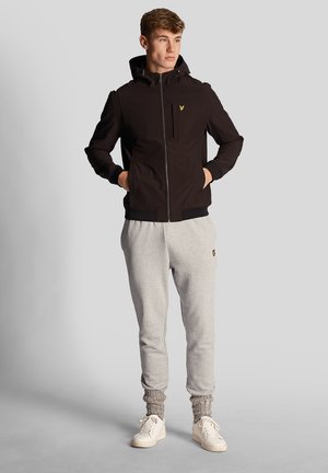 Veste zippée noire avec capuche, dotée d'une poche poitrine et d'un ourlet côtelé. Associée à un pantalon de survêtement gris clair et à des baskets blanches avec des accents texturés.