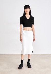 Čierny rebrovaný crop top s V-výstrihom a krátkymi rukávmi, skombinovaný s bielou rebrovanou midi sukňou so bočnou nášivkou. Čierne platformové tenisky.