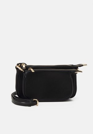 Musta nahkainen olkalaukku, jossa vetoketjulliset osastot, kullanväriset metalliosat ja ohut säädettävä hihna. Sileä pinta, minimalistinen muotoilu.