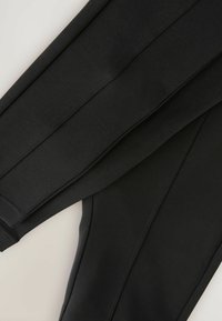 Crne atletske tajice koje se odlikuju glatkom, rastezljivom tkaninom s ravnim šavovima i prilagođenim dizajnom. Nema vidljivih uzoraka ili metalnih akcenata.