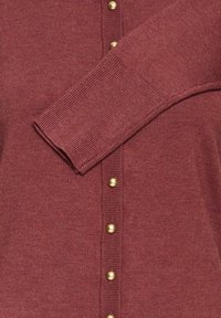 Burgunderfarbener Cardigan mit gerippter Textur, goldfarbenen Knöpfen auf der Vorderseite und gerippten Bündchen. Weicher Stoff mit figurbetonter Passform.