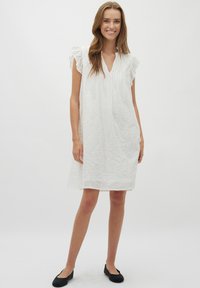 Weißes Leinenkleid mit lockerem Schnitt, kurzen Rüschensäumen und V-Ausschnitt. Verfügt über eine subtile Textur und endet knapp über den Knien.