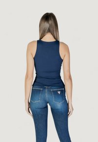 Marineblauw tanktop met een aansluitende ribbeltextuur, gecombineerd met lichtblauwe jeans met een gemiddelde taillehoogte, die subtiele achterzakken en logo-accenten hebben.