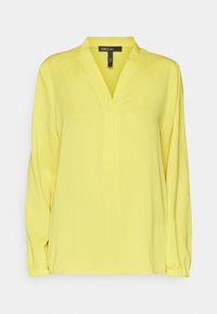 Blouse jaune à manches longues avec encolure en V, poignets élastiques et sans boutons, présentée sur un fond uni.