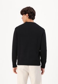 Fekete kötött pulóver kerek nyakkivágással és bordázott szegéllyel, hosszú ujakkal és texturált felülettel, hátulról nézve.