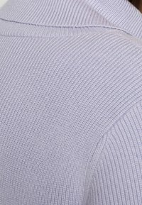 Maglione lavorato a maglia di un delicato colore viola con texture a costine e colletto ripiegato. La vista ravvicinata mette in evidenza i materiali e i dettagli del design.