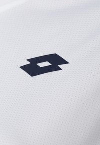 Bílá sportovní tkanina se strukturovaným vzorem a tmavě modrým logem v geometrickém designu. Centrálně umístěné logo s ostrými rysy a výřezy.