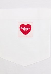Tricou alb cu un petic pătrat roz ce prezintă o inimă roșie și textul "Carhartt WIP" în alb. Material din bumbac, textură netedă.