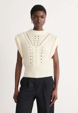 Cremfarbener Strickpullover mit Kabelmuster, kurzen Ärmeln und offenem Design. Rippbund und Schulterdetails. Kombiniert mit schwarzen Hosen.