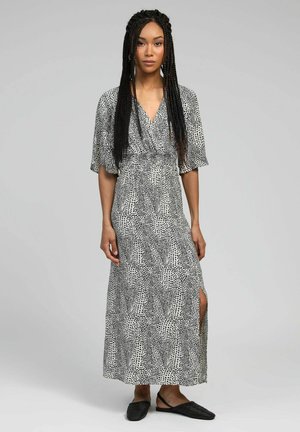 Robe maxi en noir et blanc, avec un décolleté en V, des manches courtes, des motifs géométriques et une fente sur le côté. Tissu léger avec un design fluide.