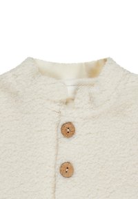 Cream-colored textured fabric with two wooden buttons, featuring a rounded neckline and soft, fuzzy surface. No visible patterns.