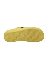 Sole gialla di calzature con gomma testurizzata, dettaglio del marchio circolare e silhouette piatta. Progettata per comfort e aderenza.