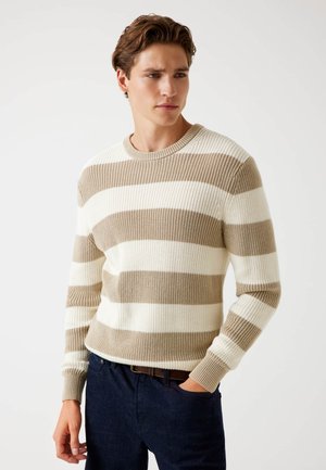 Pulover tricotat cu dungi alternative de crem și taupe, guler rotund, manșete și tiv cu nervuri; purtat împreună cu blugi negri.