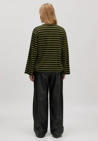 Gestreepte lange mouwen top in donkergroen en zwart, gecombineerd met brede zwarte nepleren broek. De top heeft een comfortabele pasvorm en verlaagde schouders.