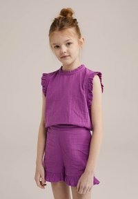Completo in lino viola composto da una blusa a maniche corte con volant e pantaloni corti coordinati con bordo arricciato. Tessuto morbido e vestibilità rilassata.