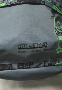 Tejido gris con gráficos temáticos de Minecraft en negro y verde. Presenta el texto: "MINECRAFT CREA, EXPLORA, SOBREVIVE" en negrita.