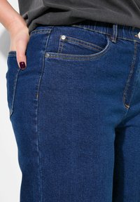 Džínové kalhoty v tmavě modré barvě se slim fit střihem, s viditelným šitím, dvěma předními kapsami a kovovým zapínáním na knoflík.