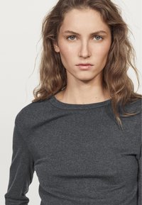 Long-sleeve, crew-neck top made of dark gray fabric. Smooth texture with a relaxed fit. Simple and minimalistic design without patterns.