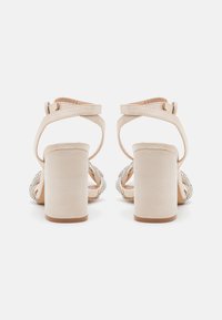 Nude høye hæl sandaler med glatt tekstur, blokk-hæl, kryssremdesign og dekorert foran med sirkulære rhinestones.