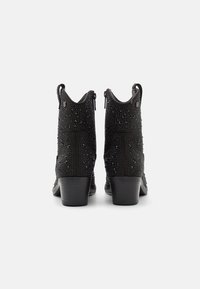 Botas de tobillo negras con parte superior texturizada que presenta tachuelas metálicas. Tienen un tacón curvado y cierre de cremallera en la parte trasera.