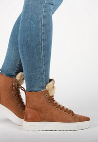 Ruske nubuk korkeakengät, joissa on tekoturkki vuori, valkoinen kumipohja ja ruskeat nauhat. Farkut ovat istuvat ja sinisestä denimmateriaalia.