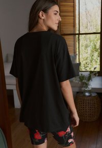 Zwarte T-shirt met korte mouwen en een losse pasvorm, gecombineerd met bloemenpatroon leggings. Houten textuur zichtbaar op de achtergrond.