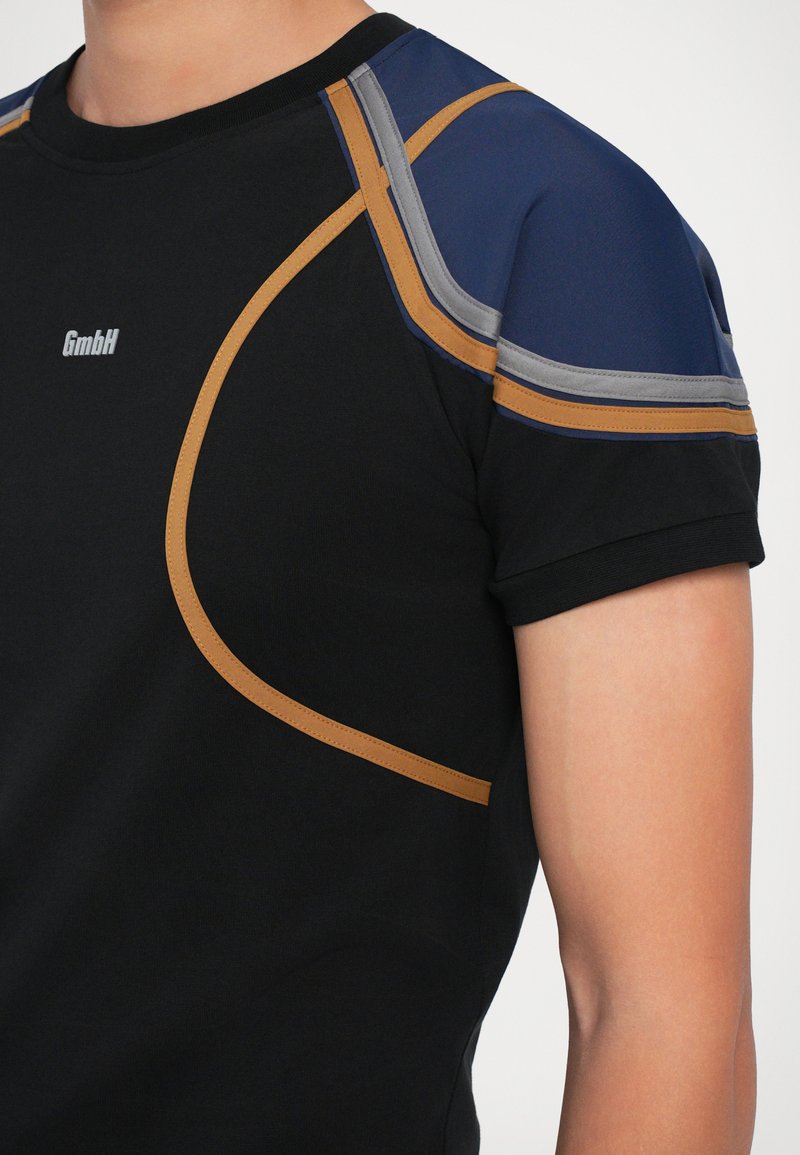 Zwarte katoenen t-shirt met blauwe, grijze en oranje accenten. Heeft een gebogen stikontwerp op de schouders en een logo op de voorkant. Korte mouwen.