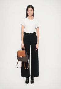 Valkoinen lyhythihainen t-paita, mustat korkeavyötäröiset leveälahkeiset farkut, mustat nilkkurit ja ruskealla yksityiskohdalla varustettu kuvioitu reppu, jossa on läppä.