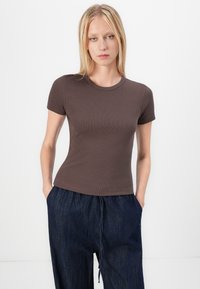 Brun ribbad kortärmad t-shirt med rund halsringning, kombinerad med löst sittande mörka denimbyxor. Tyget ser mjukt och stretchtåligt ut.