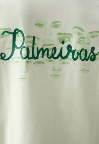 Camiseta blanca de algodón con un estampado gráfico en verde de caras humanas superpuestas y la palabra "Palmeiras" en cursiva, con una textura suave.