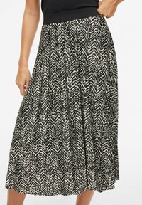 Spódnica z wzorem zygzaków w kolorze czarnym i kremowym, z szerokim czarnym elastycznym pasem w talii. Długość do połowy łydki, o lekko opływającym kroju i subtelnej fakturze.
