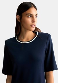 Top blu navy a maniche corte con scollatura rotonda e bordo bianco. Il tessuto sembra liscio e leggermente elastico.