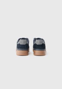 Une paire de baskets bleu marine et gris avec des semelles beige, vues de l'arrière, sur un fond blanc uni.